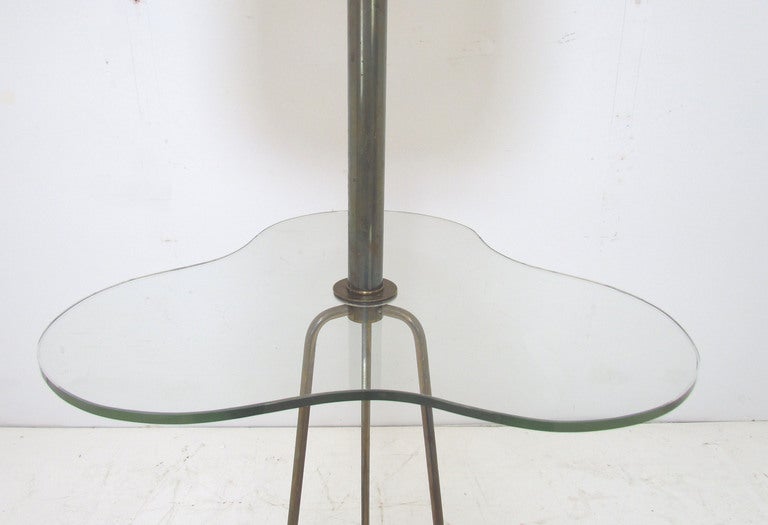 Mid-Century floor lamp with integrated biomorphic glass table top.   Base consists of tripod brass rods affixed to a ringed base, ca. 1940s. Attributed to Walter von Nessen.

In very good vintage condition with age appropriate patina to the brass