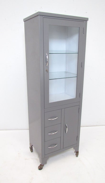 Tall industrial dispensary cabinet in steel with glass fronted door and shelves.  This locking cabinet originally used for storing controlled medicines in a clinical setting, makes a great display and storage case.   Vintage steel enamelled in
