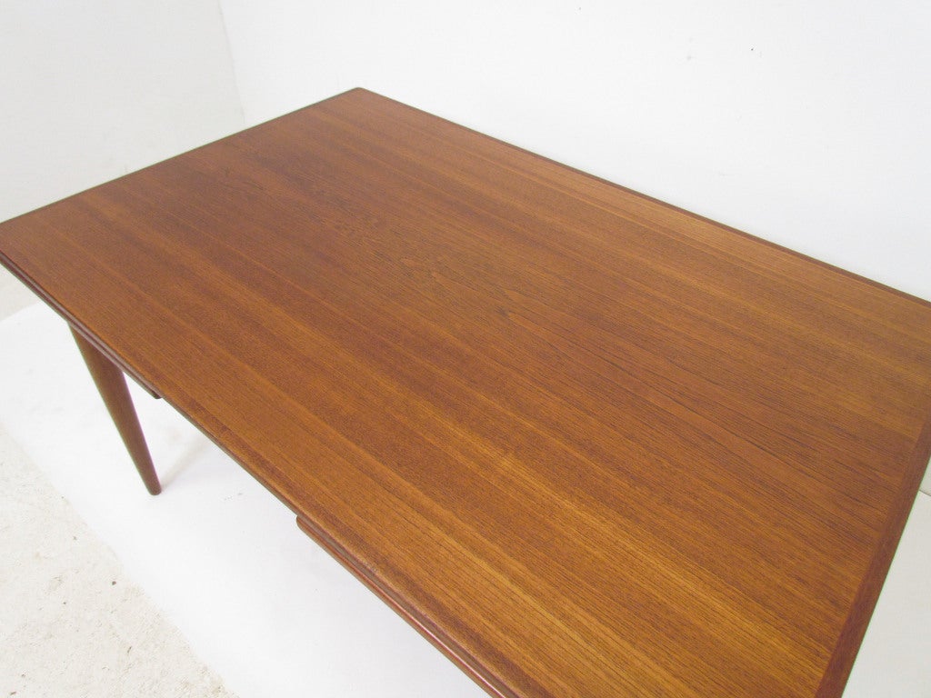 Danish teak rectangular dining table with two self storing leaves that are bookmatched to match the main table surface. Elegantly splayed legs with an arched skirt.  Measures 53