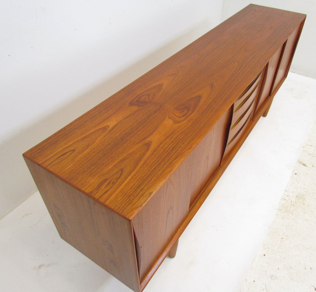 Danish teak credenza ca. 1960s, attributed to Omann Jun. Sliding bookmatched doors with carved pulls feature interior adjustable shelving. Center drawers with inset carved bowtie fronts influenced by the designs of Arne Vodder.