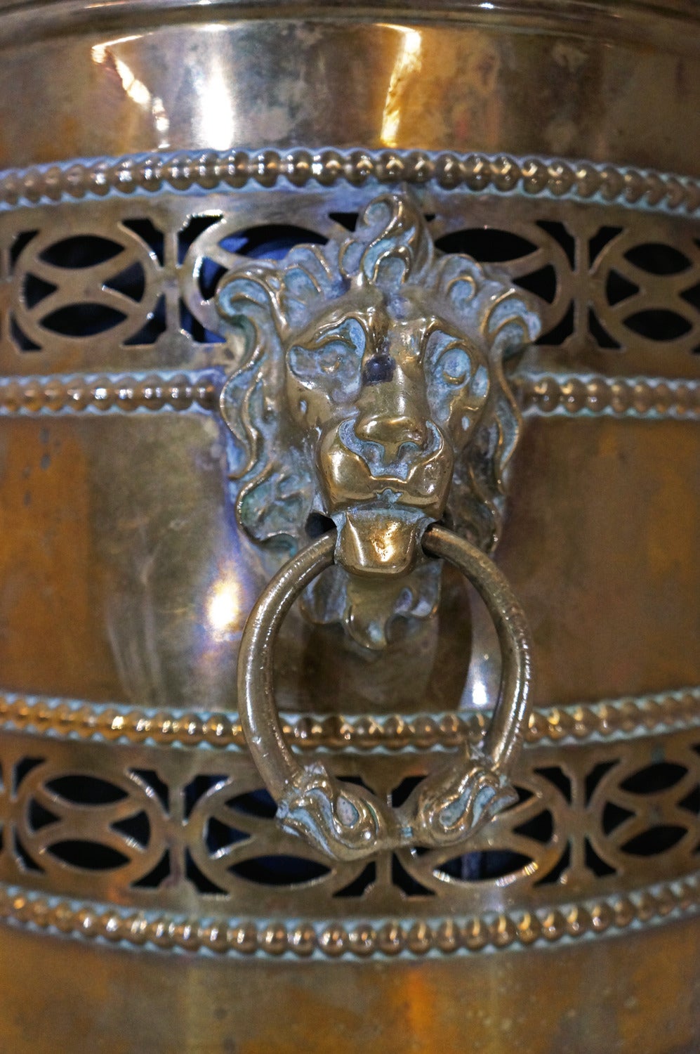 This stunning perforated brass coal scuttle is adorned with lion heads on opposite sides with a brass ring through each mouth. Removable metal insert allows for easy transport and disposal of ash and coals. 

*Not available for sale or to ship in