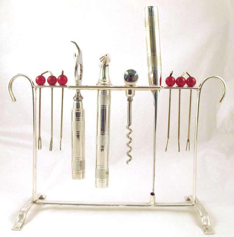 A rare and unusual cocktail bar set in the form of a rack in electro-plated nickel silver and red bakelite made by P.H. Vogel & Co., Birmingham, England. Circa 1950s.  The rack holds a series of engine-turned bar implements consisting of six