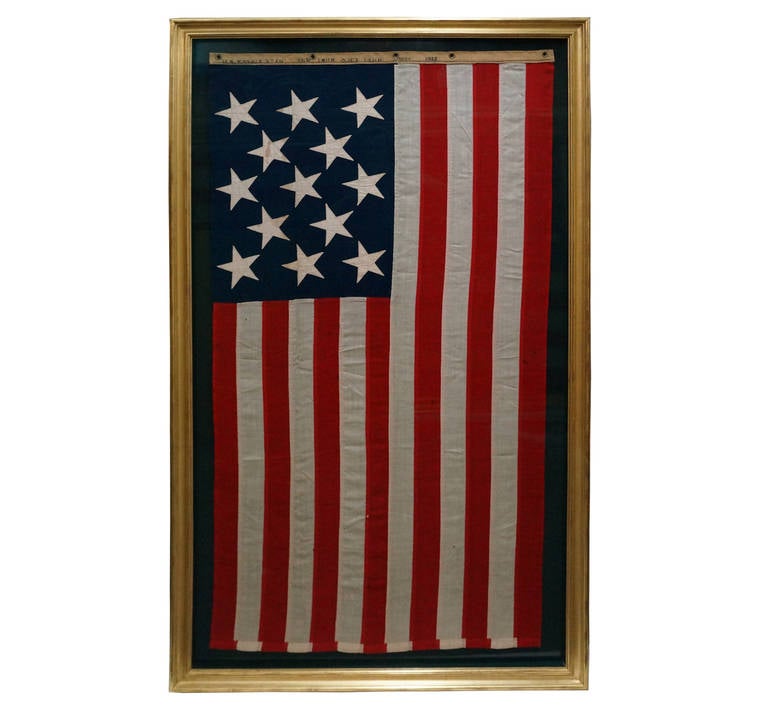 13 star American flag representing the original 13 colonies turned states. Flag trim reads, 