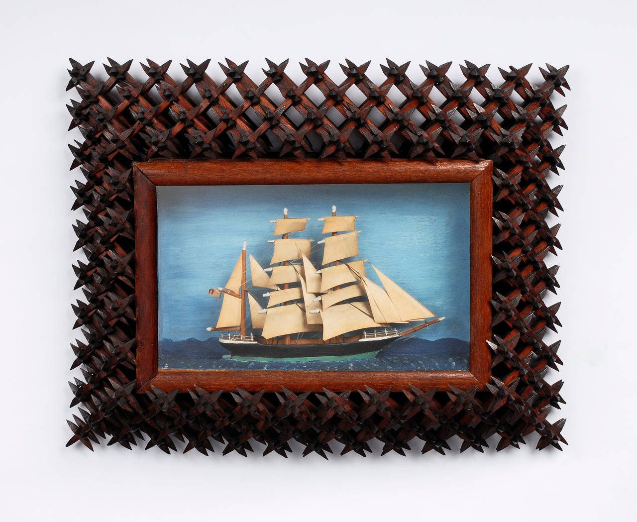 Wonderful tramp art crown-of-thorns sailboat diorama. The sailboat is mounted under glass and the boat is finely carved with three masts and folded paper sails.