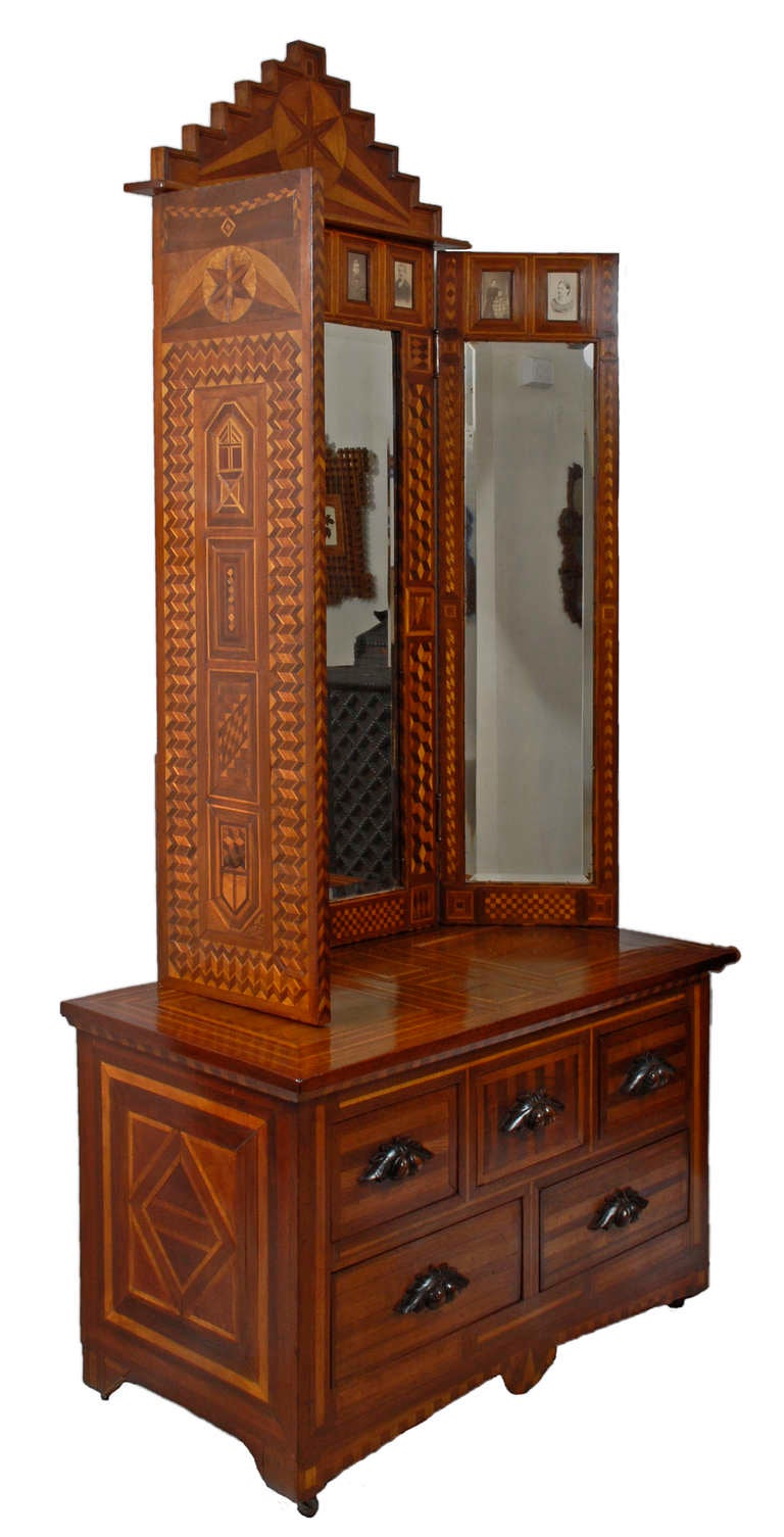 Exceptional folk marquetry stand decorated with carte de visite family photographs and a beveled tri-fold mirror. The tri-fold mirror is heavily embellished with different colored woods inlaid in various pleasing patterns including a large star on
