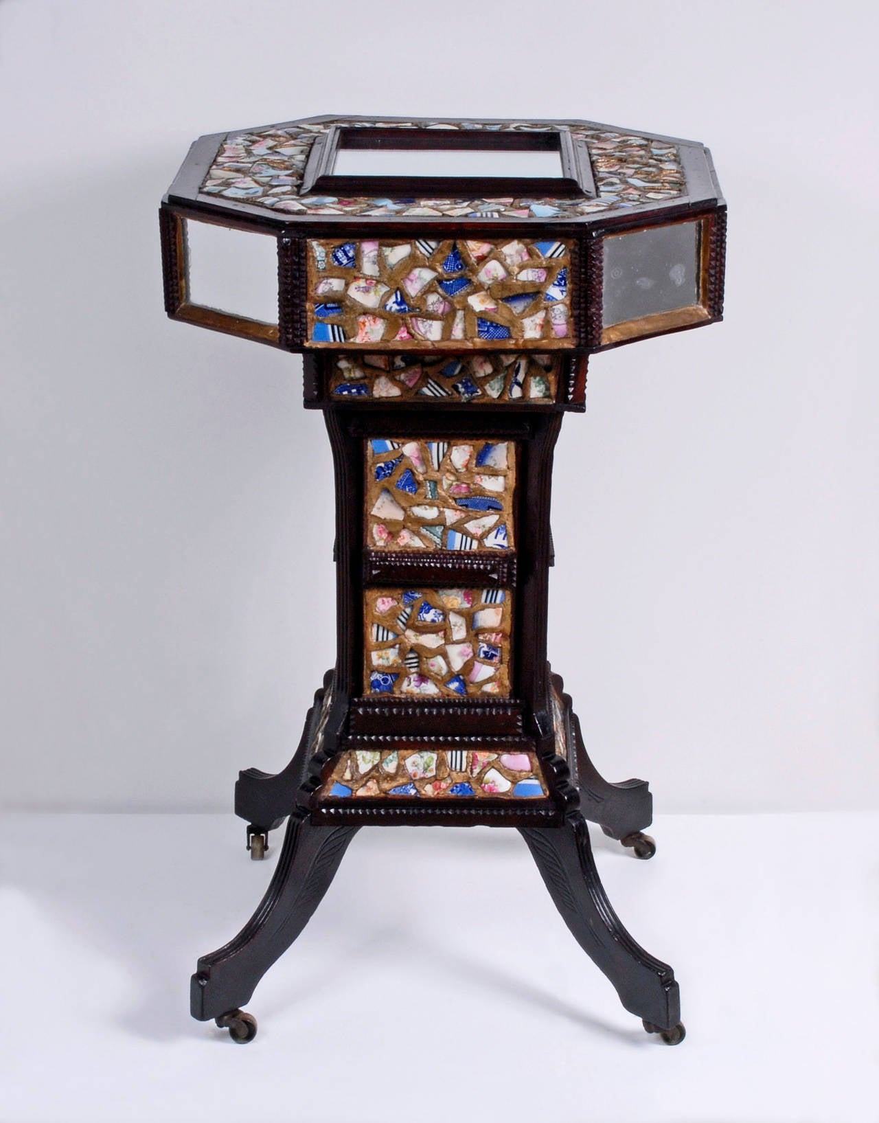 A fine Tramp Art stand with a dazzling mosaic of china shards. The Stand is eight sided with inset mirrors and is supported on slender legs incised with leaf shapes. There is a secret compartment containing a shelf hidden in the column that is