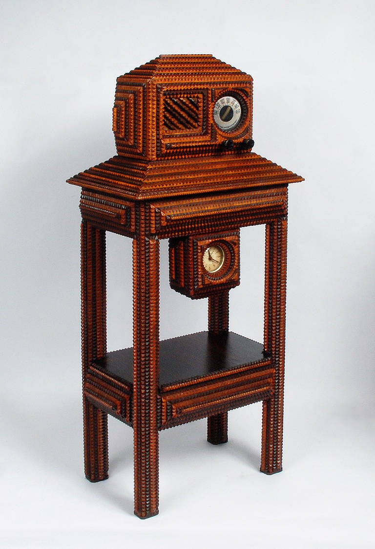 A radio in a tramp art case mounted on a tramp art stand. The radio is a working glass tube model from the 1930s and original to the piece. It is mounted in a tramp art case and sits on a tramp art stand. There is a clock attached to the stand. The