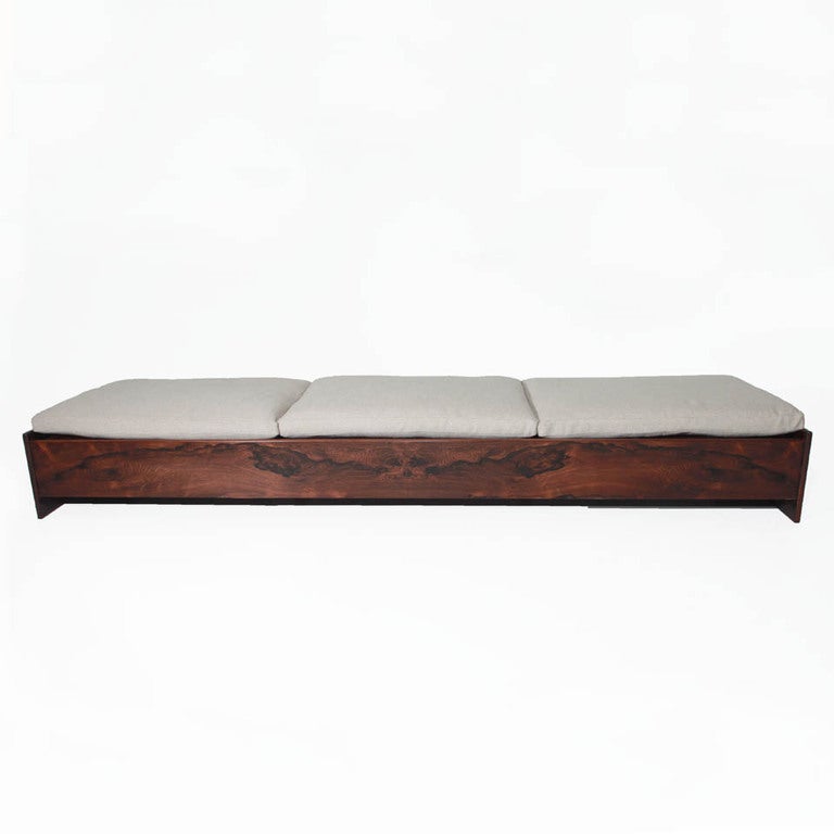 A low Rosewood bench or day bed from Brazil. Under three newly constructed cushions upholstered in natural linen is individual slats of beautifully grained Rosewood. Each large side panel has the same beautiful wood grain.

Many pieces are stored