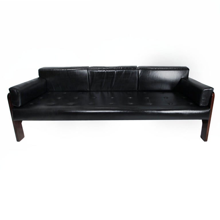 A leather and rosewood sofa from Brazil. The seat cushion is tufted and all cushions have been newly reupholstered. The rosewood panel on both sides has rounded cutouts at the bottom, making four legs rather than being full sideboard supports. Seat