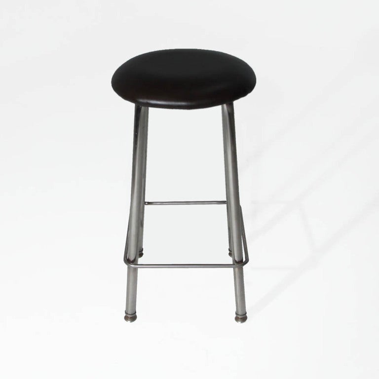 A set of seven chrome and dark brown leather button stools on four solid legs with feet. Price is per stool and stools are available in black and tan leather (total of 13).

    