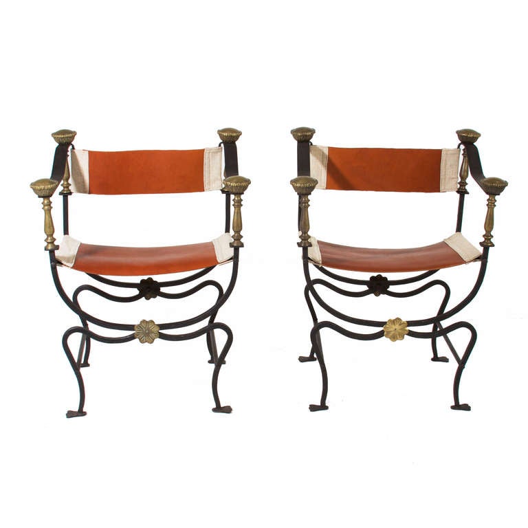 A pair of hand-forged steal & brass campaign chairs with ornate details and caramel leather and cream linen sling seats and backs. 

Seat Depth: 14