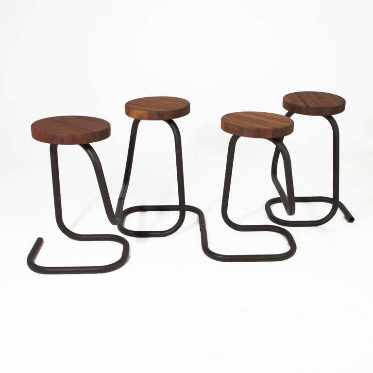 A set of four bronze finished bar stools with curving metal tube bases and solid laminated Walnut seats with a flat oil finish.

     
