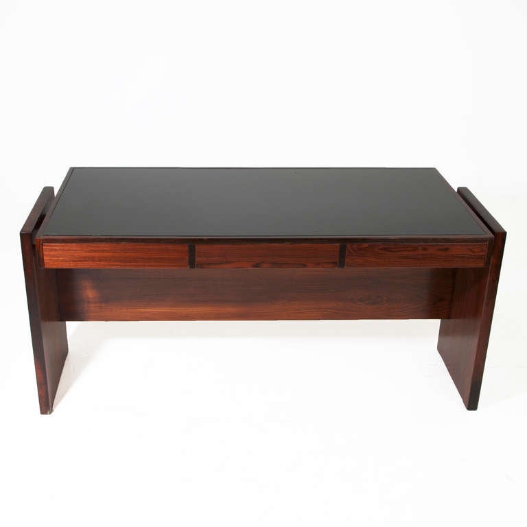 Rosewood desk designed by Brazil's Joaquim Tenreiro with a black reverse painted glass top and three drawers. This desk came from the Bloch, Editores headquarters, a building designed by Oscar Niemeyer and with interiors furnished by Sergio