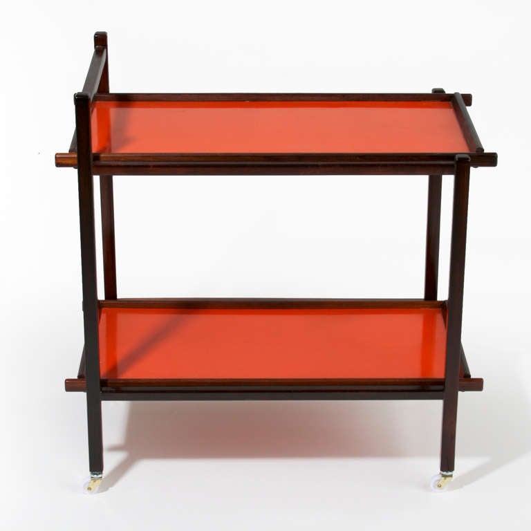 A lovely vintage exotic dark grain wood serving cart, tea cart, or bar cart from Brazil by Sergio Rodrigues for OCA with two removable red melamine trays that slip easily in and out of the frame. The all original wheels are white.

 