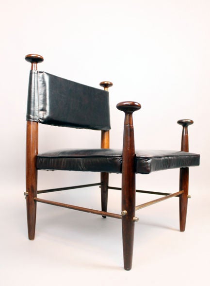 A pair of solid walnut chairs with sculpted detailing, original patinaned metal supports, and  black leather upholstery with reddish undertones.  Chairs are large as side chairs but can not be considered lounge chairs.