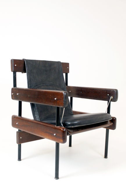 A pair of interesting solid Baruna wood chairs with black leather sling seats and metal frames designed by Brazil's Sergio Rodrigues. The seat is slung in such a way that it has a slight rocking motion when you are seated. This chair was originally