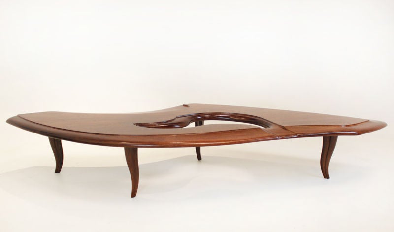 A stunning low coffee table in walnut with sculptural legs and a hollowed center designed by Ray Leach.
We are pleased to present this exquisite collection of restored sculptural wood furnishings by little-known California designer Ray Leach. The