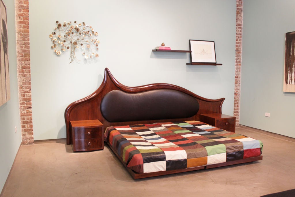 A carved solid walnut king sized platform bed with black leather upholstered headboard and attached walnut night stands by Ray Leach. Leather patchwork shown in pictures and mattresses not included.<br />
Side table measurements:<br />
Height: