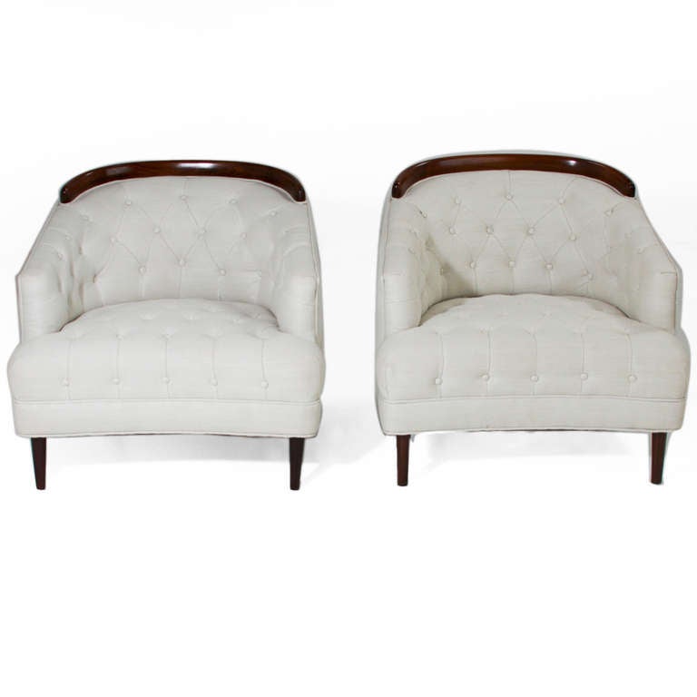 Pair of Classic low armchairs upholstered in a clean, tufted cream linen with solid dark mahogany sculptural trim on the backs. The front legs are conical mahogany, and the back legs have original chrome casters.

Measure: Seat depth measures