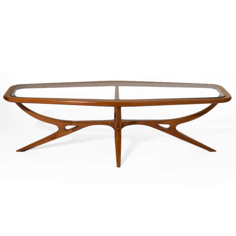 A sculptural glass coffee table by Guiseppi Scapinelli in Peroba de Campos. The legs very elegantly spider inward and cruciformly connect in the center with two peep holes on either side. The elongated hexagon shape of the top mirrors this design.