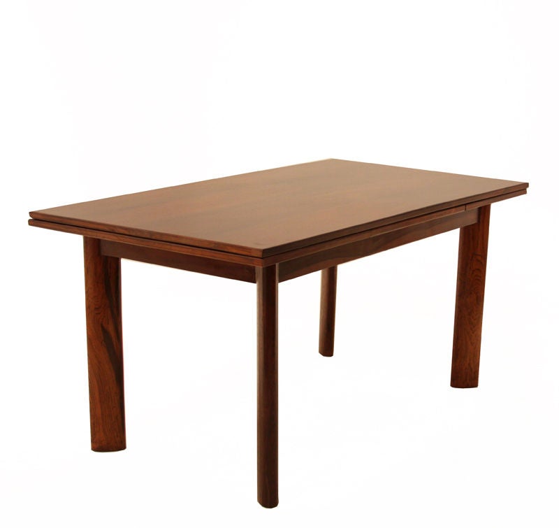 This beautiful dining table by Jean Gillon shows a magnificent rosewood grain pattern and is simply yet excellently conceived and executed. It has two leaves (each 20 inches wide) that slide out from under the top on either end to make a longer