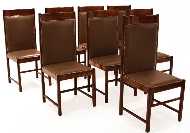 Set of 8 beautiful high back chairs by Celina Moevis made with solid Rosewood and a high quality supple brown leather. There are bronze tacks that surround the leather seats and backs.  The two sets are slightly different in that the chair backing