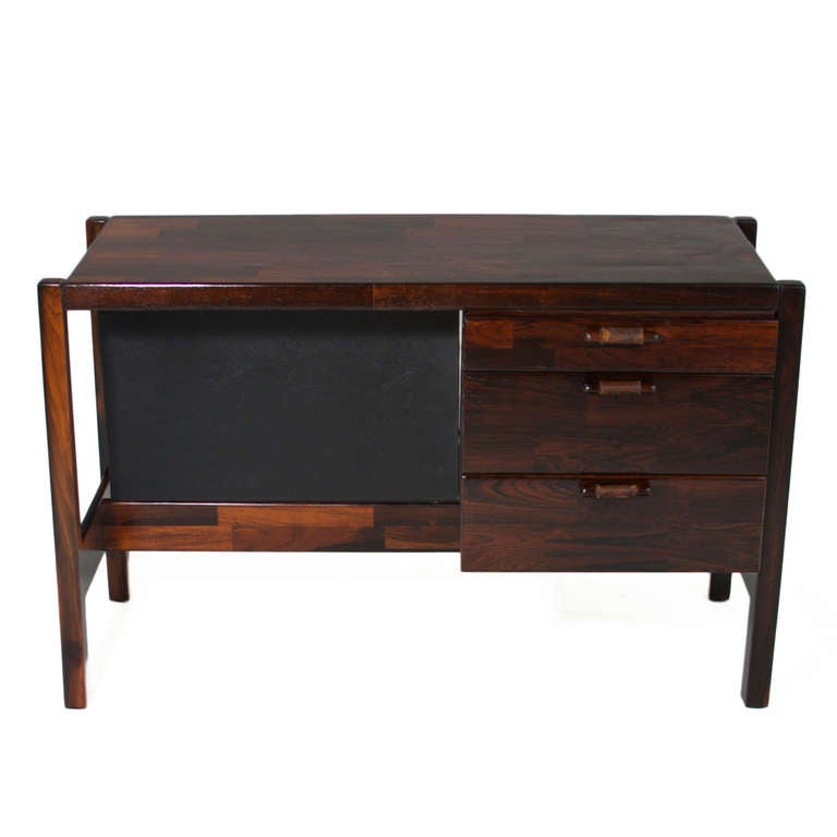A smaller version of the classic desk design by Jorge Zalszupin in solid patchwork rosewood. The desk has three drawers with rosewood pulls wrapped in the original aged leather. The inside of the drawers are white laminate and are in original