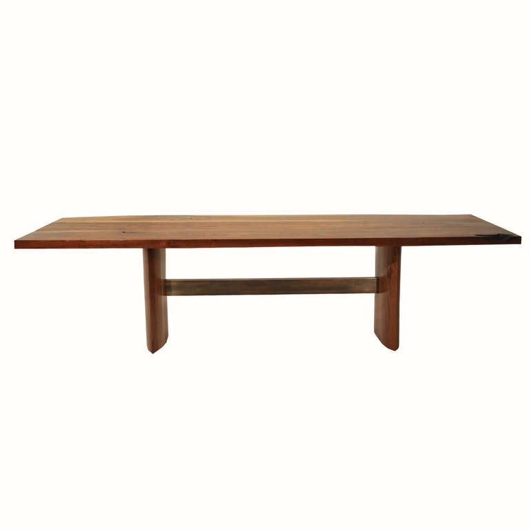A solid Walnut dining table by Thomas Hayes Studio with the stretcher made of the highest grade architectural bronze. Legs are made of solid stacked laminate Walnut and are eye shaped. The wood has the beautiful features of old wood, with figural,