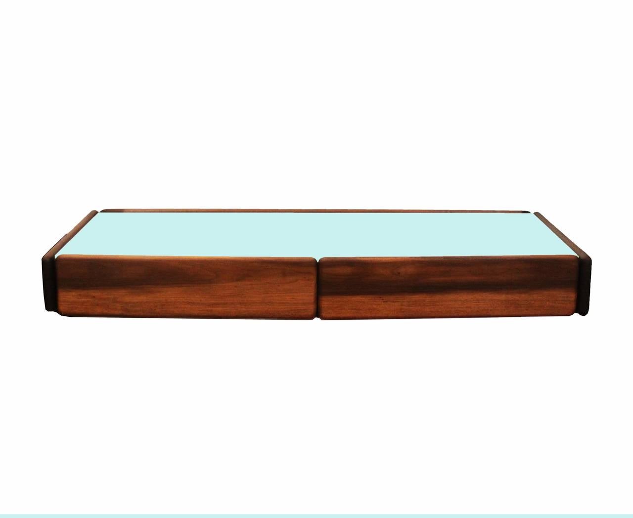 A floating shelf in Brazilian hardwood with two drawers and inset reverse painted white glass that appears almost light green through the glass, designed by Celina Moveis. The wood has been refinished with a clear oil finish that brings out the