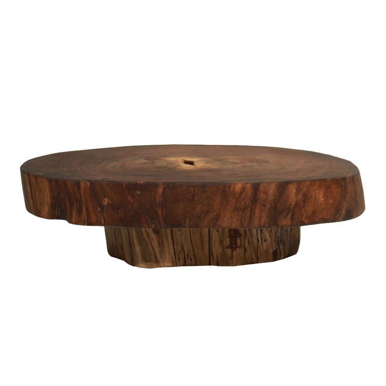 A solid Tamboril tree round coffee table with live edges on a smaller pedestal base. 