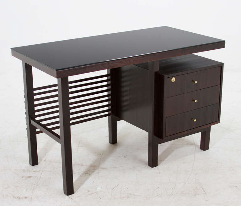 A small Brazilian Pinho de Riga desk with brass pulls and lock and a reverse painted black glass top. 

Many pieces are stored in our warehouse, so please click on 