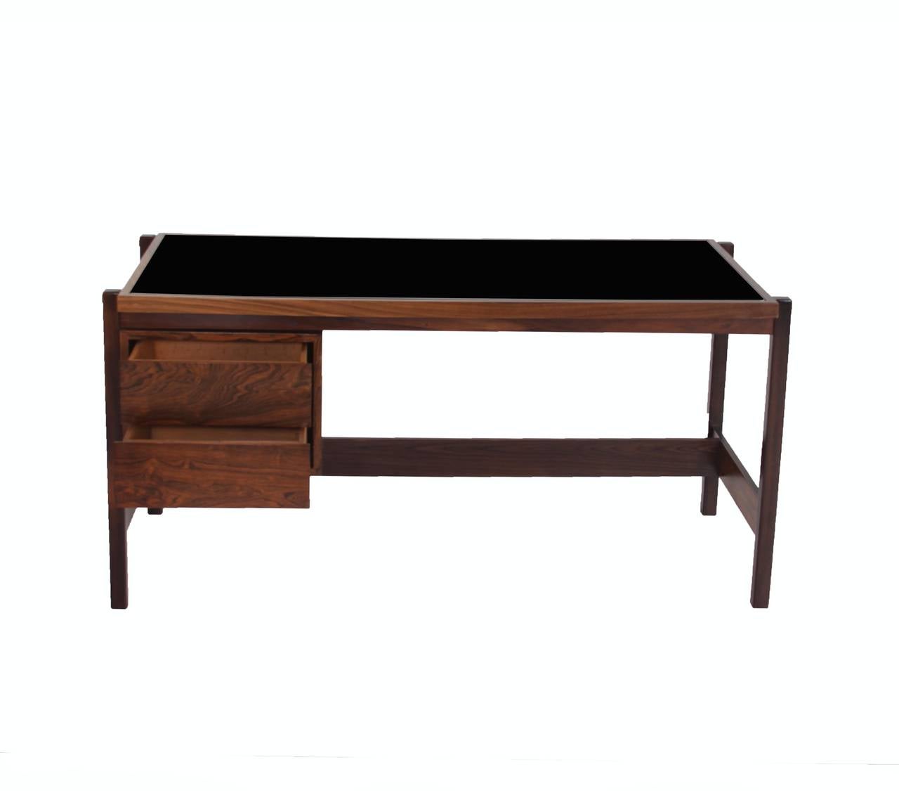 A solid Caviuna Wood desk from Brazil with two drawers, reverse painted black glass top designed by Sergio Rodrigues. 

Many pieces are stored in our warehouse, so please click on 