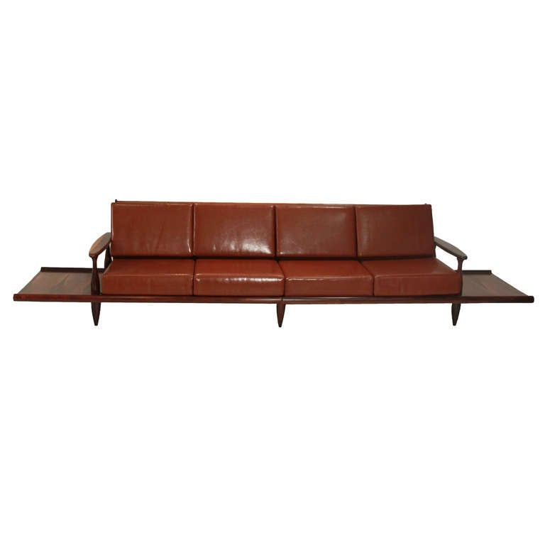 Unique Brazilian Rosewood sofa with attached side tables also in Rosewood. The upholstery is original in a reddish brown leather and the Rosewood arms and feet are sculptural and elegant. 

Length of just sofa:
Length with side tables: 142