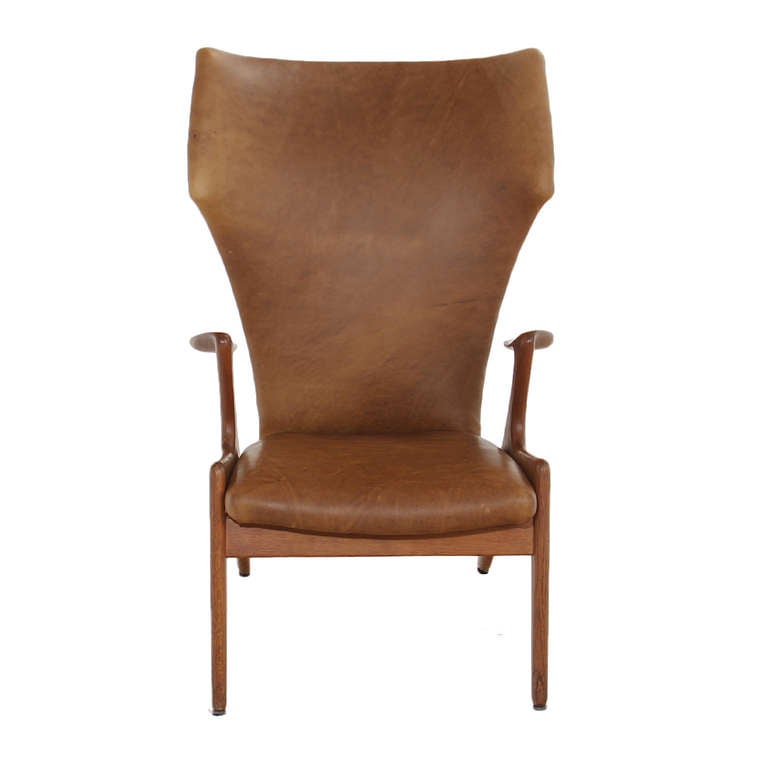A stunning lounge chair by Kurt Ostervig in solid oak with soft carmel leather upholstery. The design is curvaceous, the head rest is fairly wide and curves inwards. The back of the chair narrows in creating a sculptural look. The arms are scooped