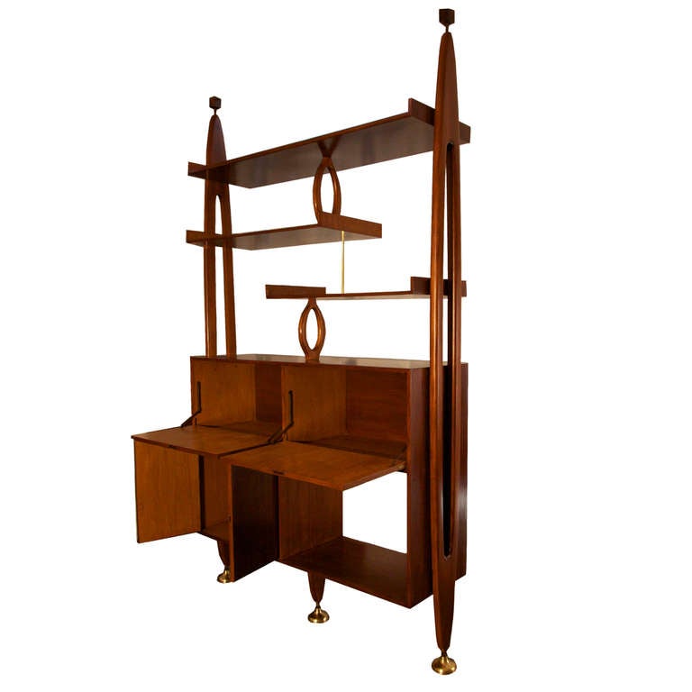 A large and versatile storage piece made out of Brazilian Freijo wood that can function as a room divider or wall unit. It is supported by 3 large brass feet on the floor and wood blocks at the top that connect to the ceiling. It is composed of