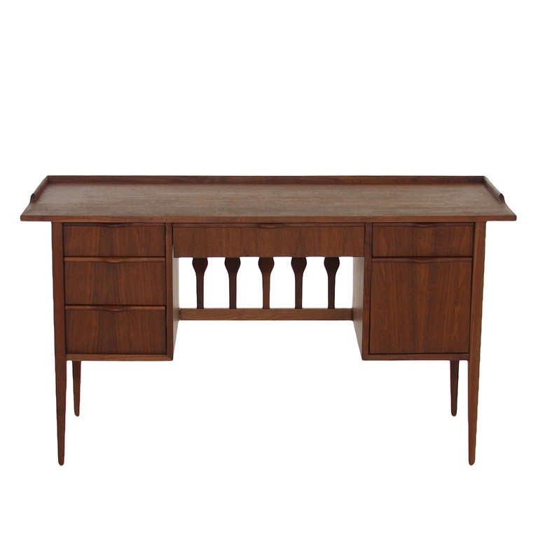 A desk in solid Walnut by Glenn of California. This desk has a very minimalist look to it, the legs are conically shaped. There are a total of six drawers all at different sizes for various purposes. There is a beautiful detail on the back of the