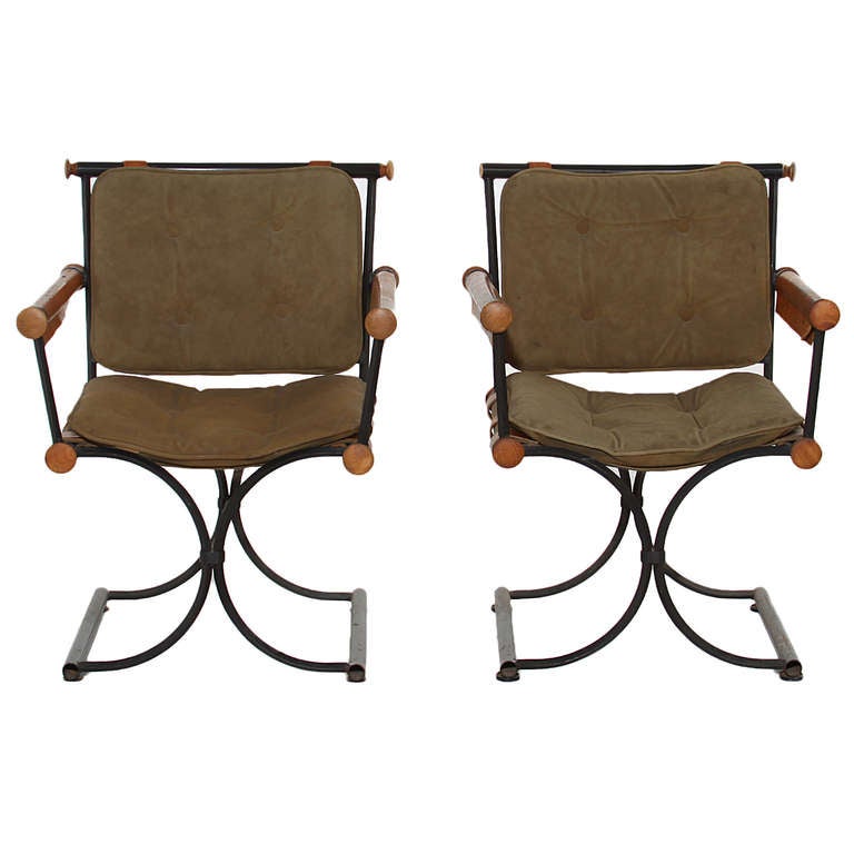 A pair of elegant chairs by Cleo Baldon in completely original condition. The frames are black iron and have wood and leather details. The arms are wood rounds wrapped in a thick caramel leather, and the seat and back is upholstered in a green