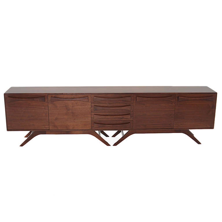 A long credenza with elegant but sturdy double sculptural base in solid Walnut and solid Walnut bow-tie pulls by Thomas Hayes Studio. There are four drawers in the center and four doors which open to ample storage. Drawers are made with the highest