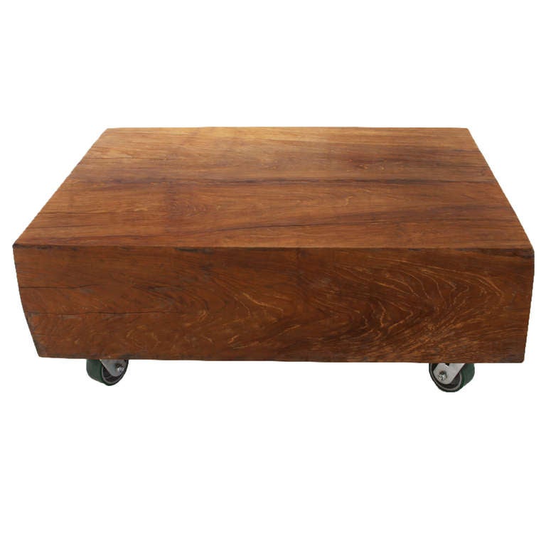 A stunning vintage coffee table made from a huge chunk of solid Teak with large casters as feet. The wood has been cleaned thoroughly but not completely refinished, and the finish is a soft satin lacquer that highlights the grain but is not too