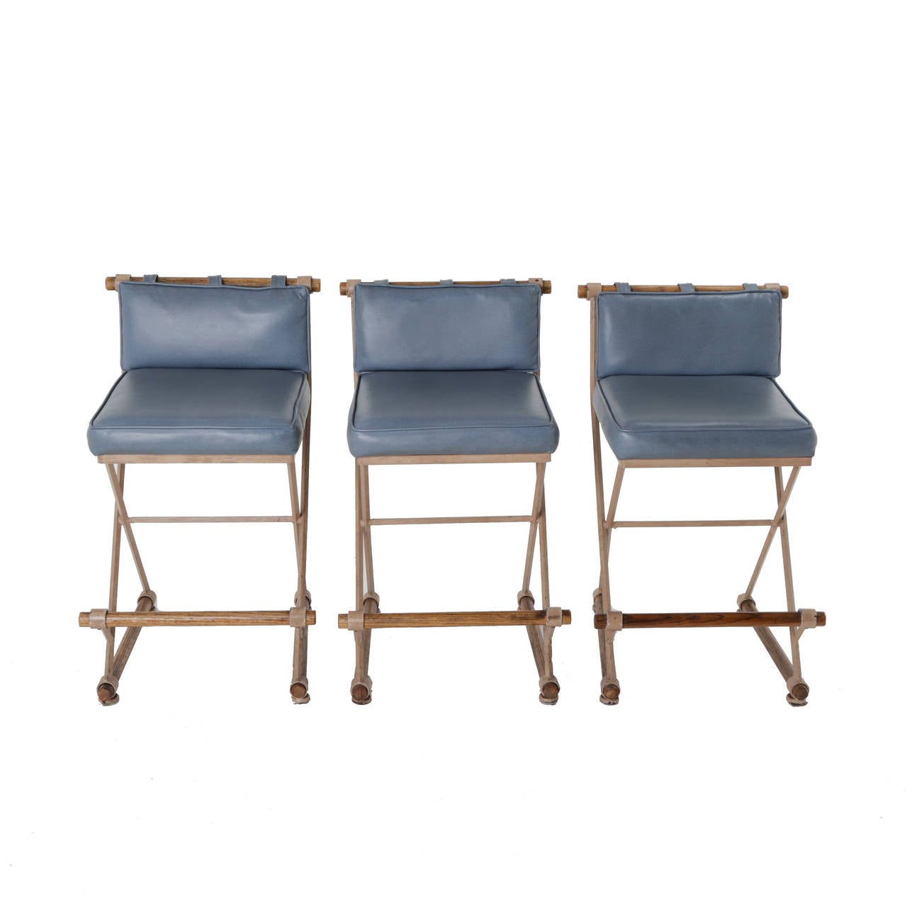 Three campaign style stools by Cleo Baldon with painted wrought iron bases and solid Oak dowel footrests and details. Upholstered in Blue Vinyl; Counter Height.

Many pieces are stored in our warehouse, so please click on CONTACT DEALER under our