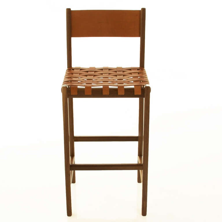 A sturdy solid stool by Thomas Hayes Studio with a seat of woven leather straps and back of solid leather panel with brass details on the back. 

This item is available for custom order and the lead time is 6-8 weeks; sometimes we are able to