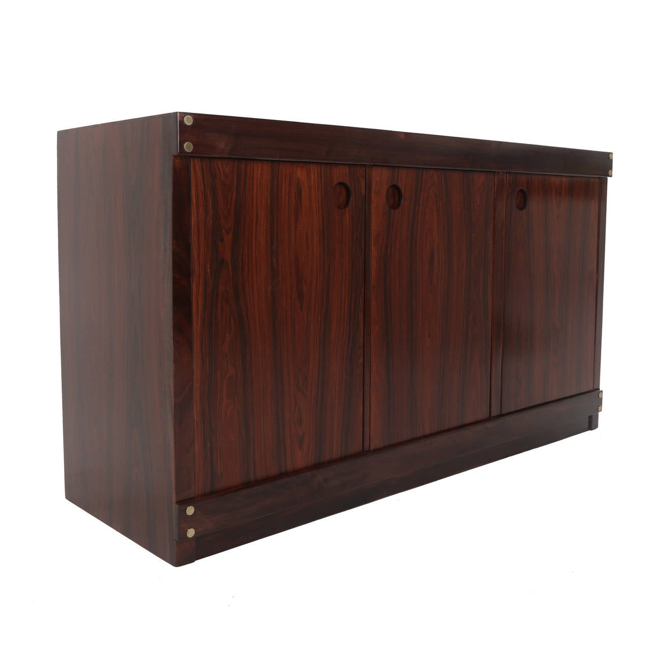 A stunning three-door rosewood credenza or sideboard from Brazil, designed by Sergio Rodrigues. Featuring new black glass top, inset circular pulls and brass plug details. Finished in satin lacquer.

Many pieces are stored in our warehouse, so
