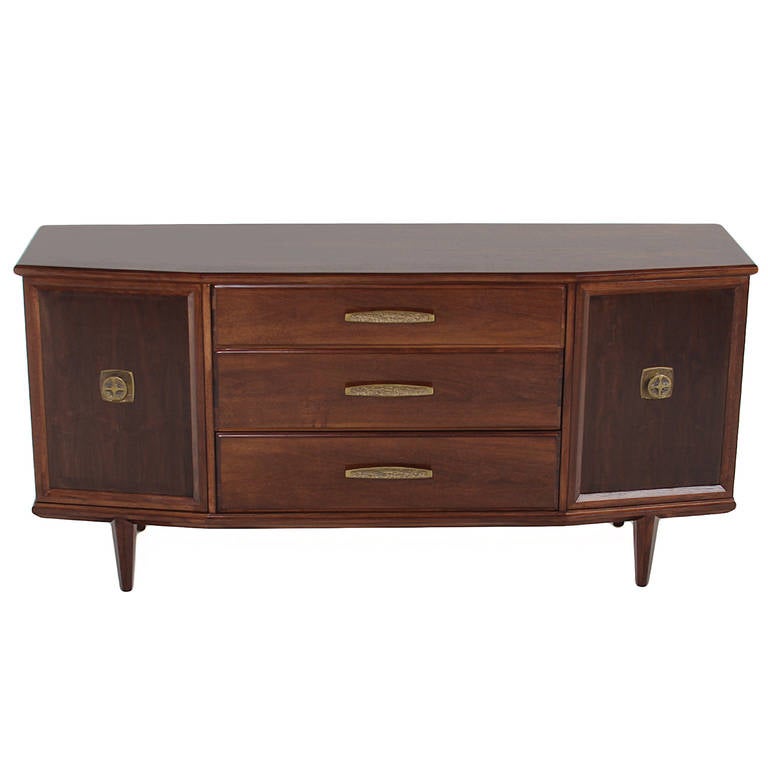 Beautiful angular walnut buffet with original ornate bronze hardware. The top drawer is lined with felt and is separated into sections, and the elegant angles of the credenza are echoed in the four tapered legs.

 