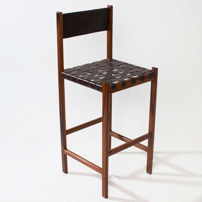 A sturdy solid Rosewood bar stool by Thomas Hayes Studio with a seat of leather straps and back of solid leather panel with patinated brass details on the back. 

This item is available for custom order and the lead time is 6-8 weeks; sometimes we