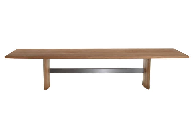 Oak dining table by Thomas Hayes Studio with a chrome-plated steel stretcher. The double pedestal eye-shaped legs are made of solid stacked laminate wood. 

It is available for custom order in other sizes, woods and finishes, or alternately with a
