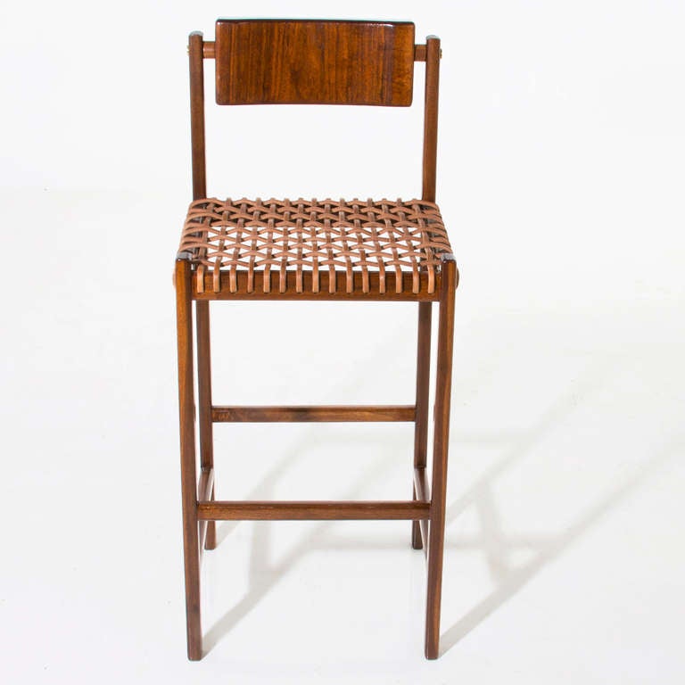 A sturdy solid Walnut bar stool with a seat of thin leather straps and back of carved solid Walnut that pivots for ultimate comfort and brass plug details on the back by Thomas Hayes Studio.

This item is available for custom order and the lead