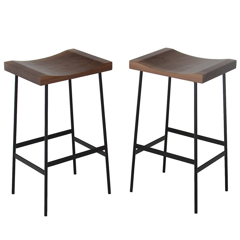 Flat black finished steel bar stools with solid carved figural Walnut seats by Thomas Hayes Studio. 

This item is available for custom order and the lead time is 6-10 weeks; sometimes we are able to complete projects faster, so please contact us