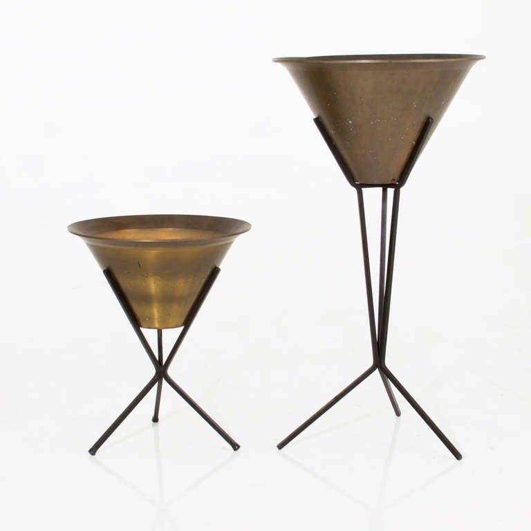 Pair of vintage patinated brass planters attributed to Paul McCobb on black iron tripod stands. The planters are conical and have a lip, and show beautiful patina consistent with age and use.

Many pieces are stored in our warehouse, so please
