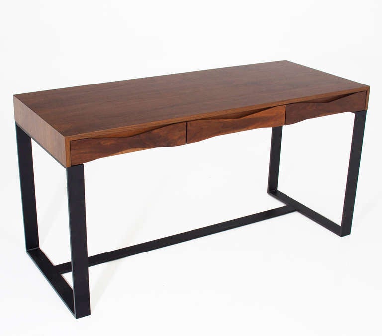 A walnut desk by Thomas Hayes Studio with three drawers with sculptural solid Walnut bow tie details that also acts as pulls. The top sits upon a frame of flat black finished solid steel base. Desk is heavy and sturdy. Drawers have soft close