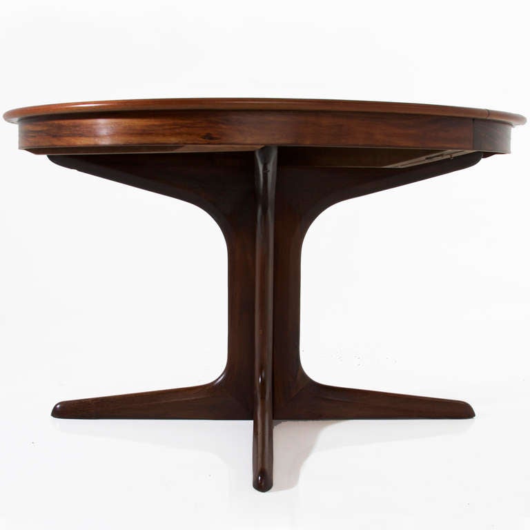 A stunning Danish Modern extendable dining table in Rosewood by Koefoeds-Hornslet. Without leaves, the table is round, and with leaves, it has an elegant racetrack shape. The pedestal base with 4 sculpted feet separates when the leaves are